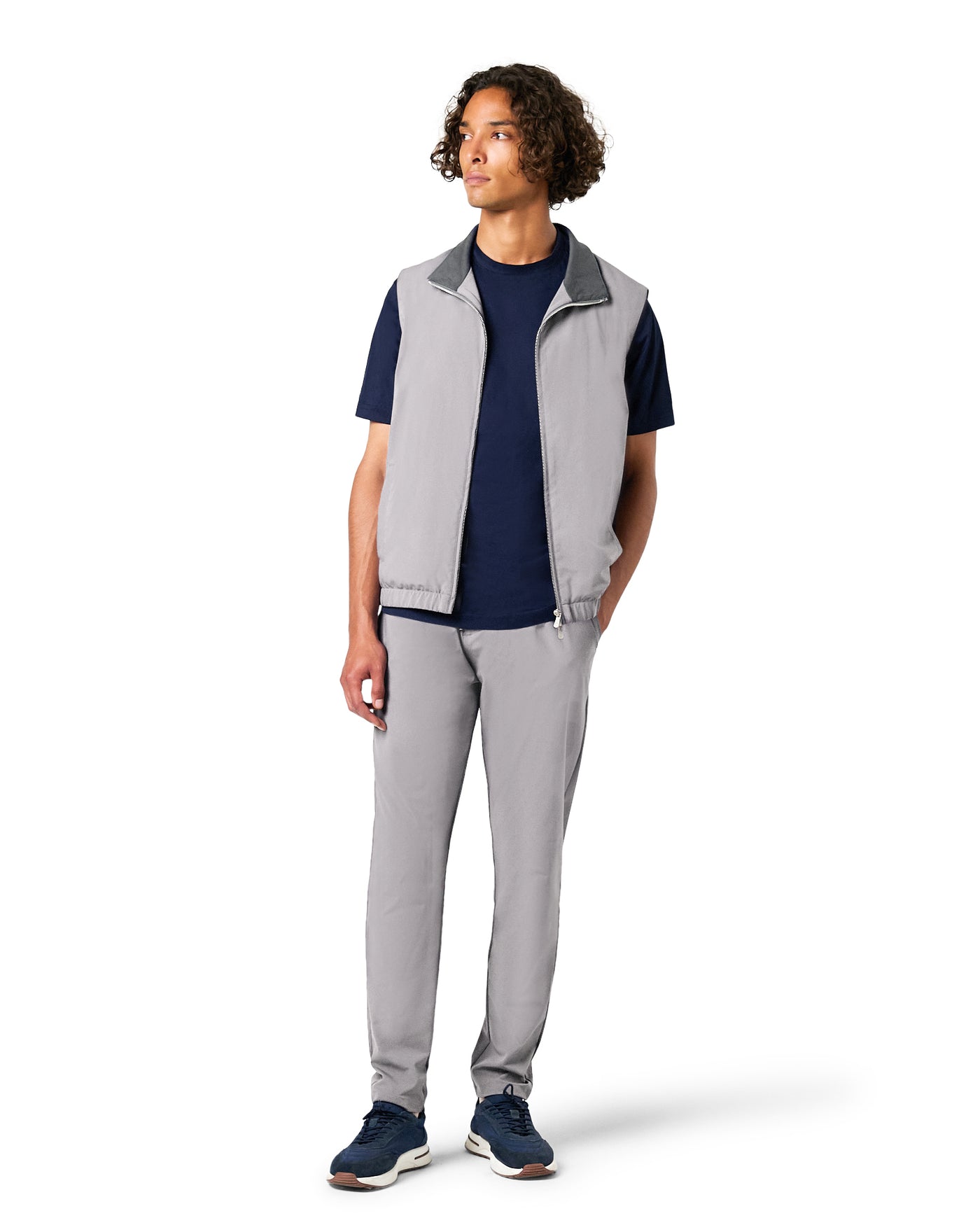 Person wearing a gray vest over a navy shirt with gray pants on a white background