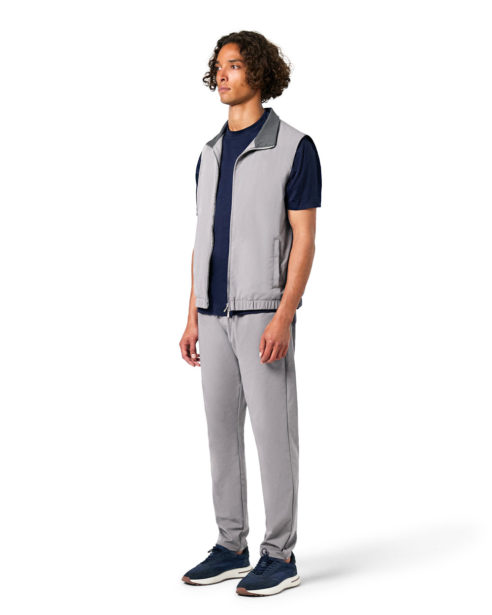Man wearing a gray vest over a navy shirt with gray pants on a white background