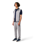 Man wearing a gray vest over a navy shirt with gray pants on a white background