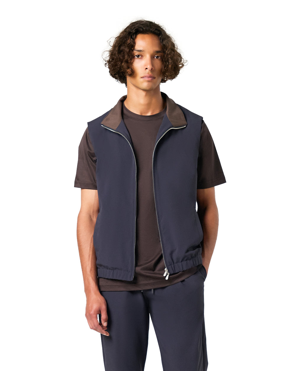 Man wearing a navy vest over a dark shirt on a white background