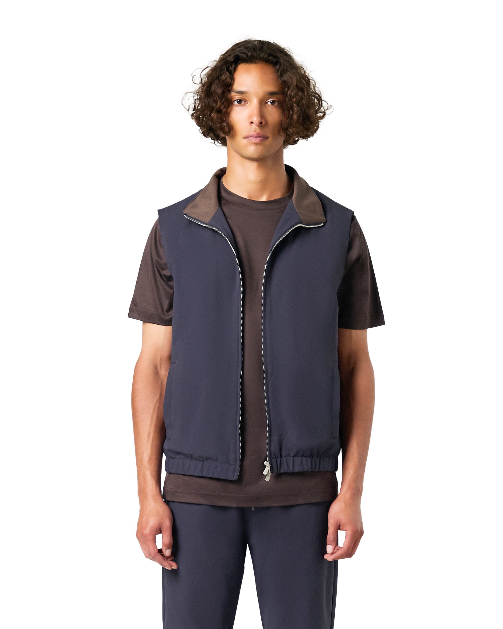 Man wearing a navy vest over a brown shirt on a white background