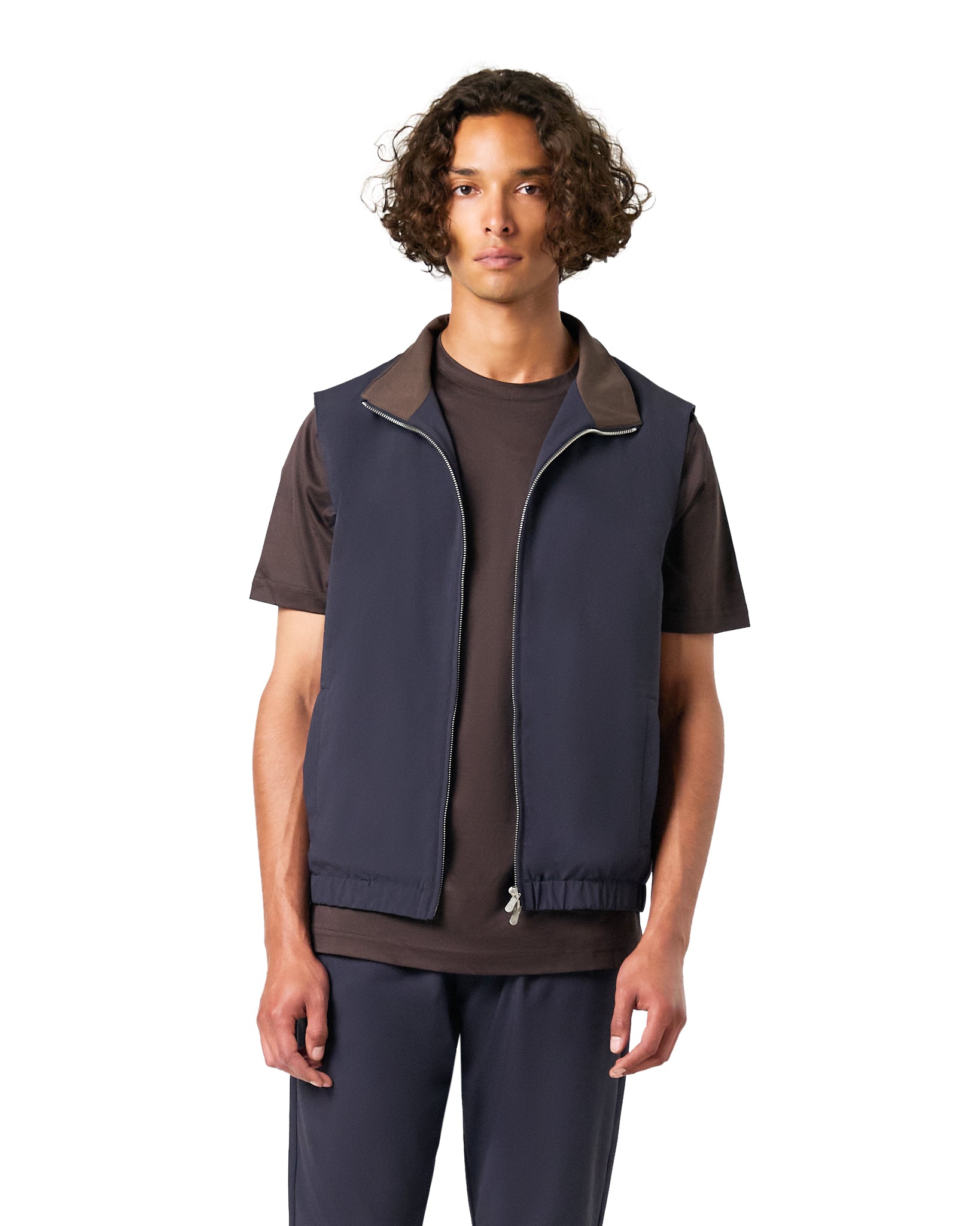 Man wearing a navy vest over a brown shirt on a white background