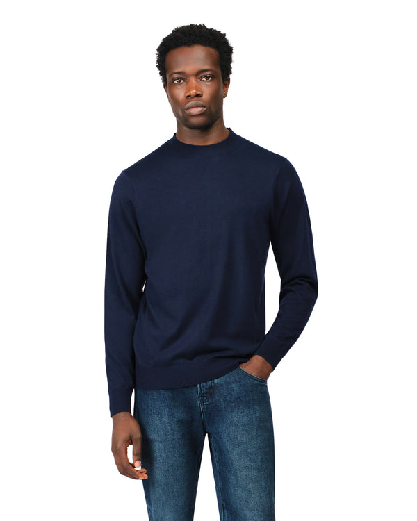 Man wearing a navy sweater and blue jeans on a white background