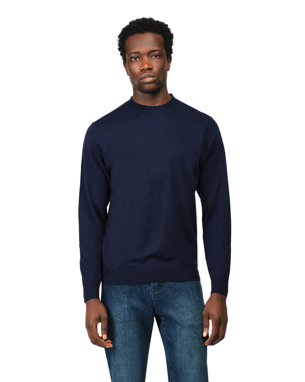 Man wearing a navy sweater and jeans on a white background