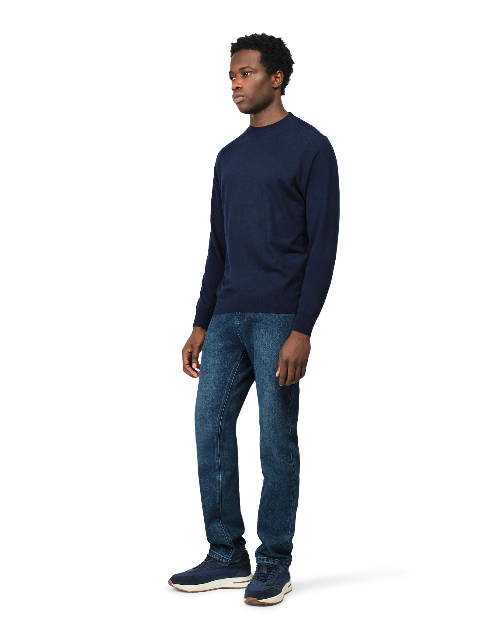 Man wearing a navy long-sleeve shirt and blue jeans on a white background