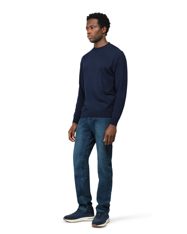 Man wearing a navy long-sleeve shirt and blue jeans on a white background