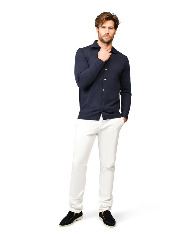 Man wearing a navy blue shirt and white pants on a white background