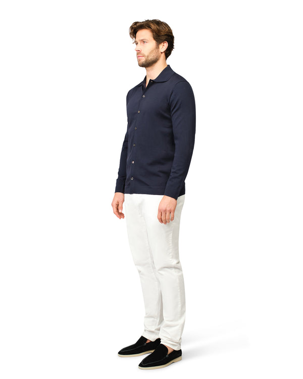Man wearing a navy button-up shirt and white pants on a white background