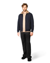 Man wearing a navy jacket with a beige collar and black pants on a white background