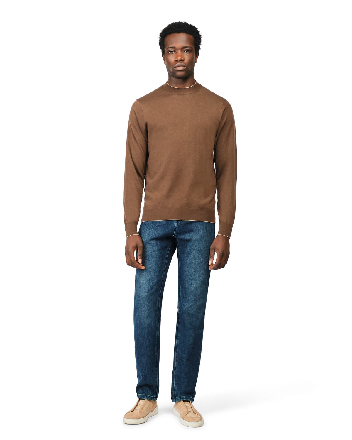 Man wearing a brown sweater and blue jeans on a white background