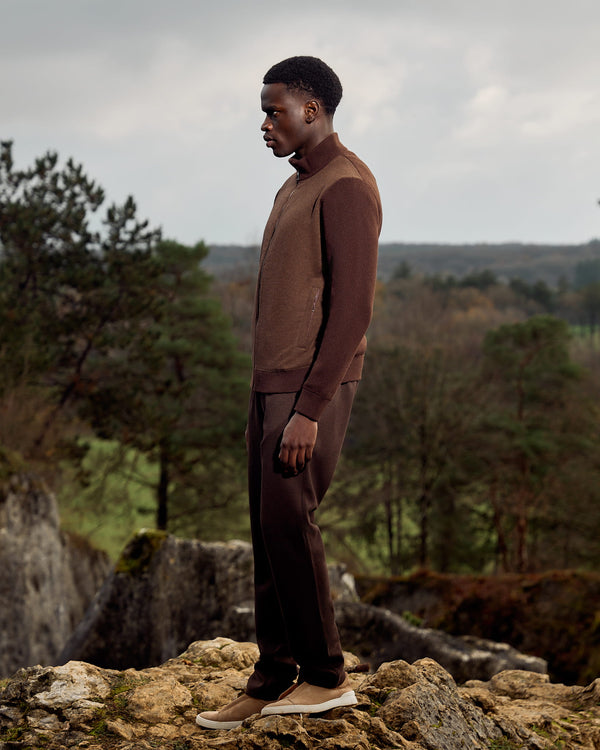 Man in a brown outfit standing on rocks with a forest background