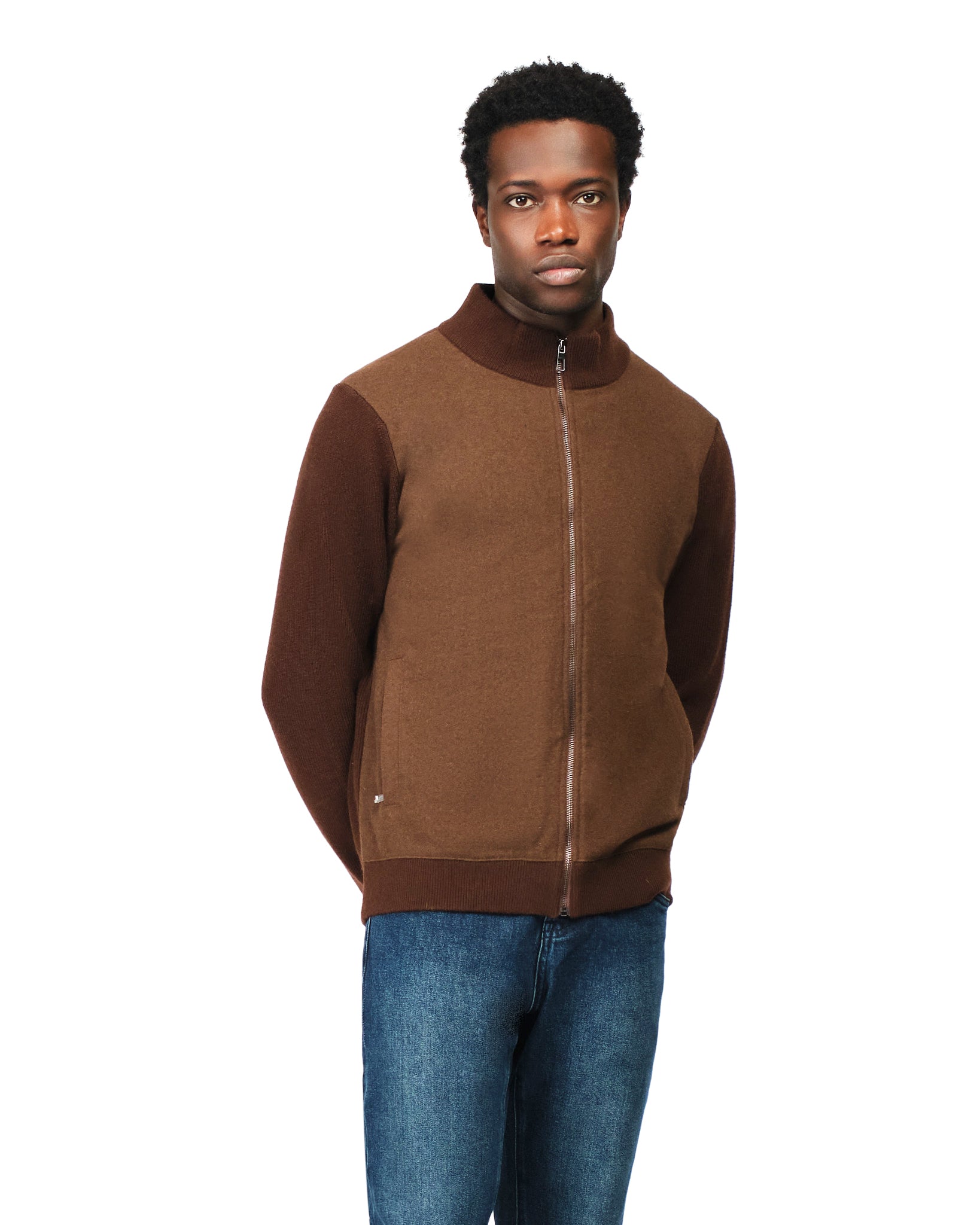 Man wearing a brown zip-up sweater over a beige shirt with blue jeans on a white background