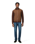 Man wearing a brown jacket and blue jeans on a white background