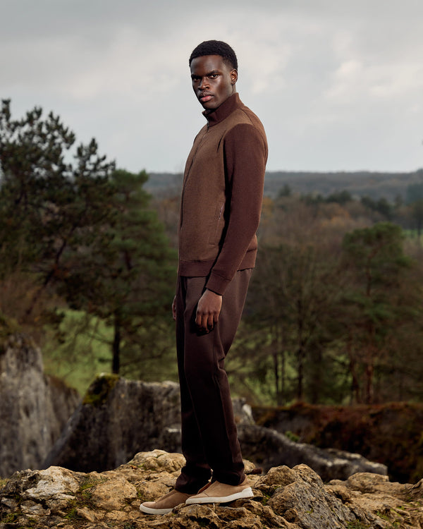 Man in brown outfit standing on rocky terrain with a forest background
