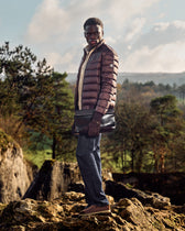 Man standing on a rocky outcrop with trees and mountains in the background