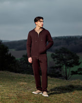 Man wearing a brown tracksuit standing on a grassy hill with a scenic background