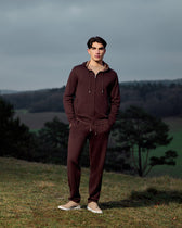 Man wearing a maroon tracksuit standing in a field with trees and a cloudy sky.