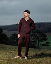 Man wearing a maroon tracksuit standing in a field with a scenic background