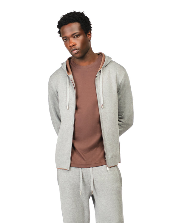 Man wearing a gray hoodie and pants with a brown shirt underneath on a white background