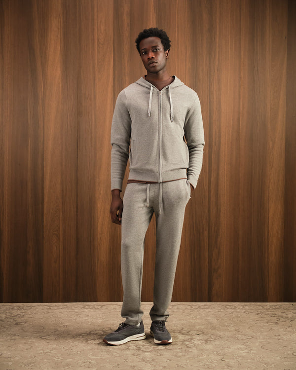Man wearing a gray hoodie and pants against a wooden paneled wall.