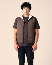 Man wearing a brown vest over a dark shirt on a beige background