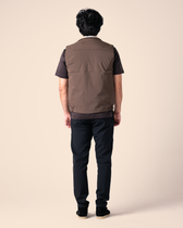 Person wearing a brown vest over a black shirt and pants on a beige background