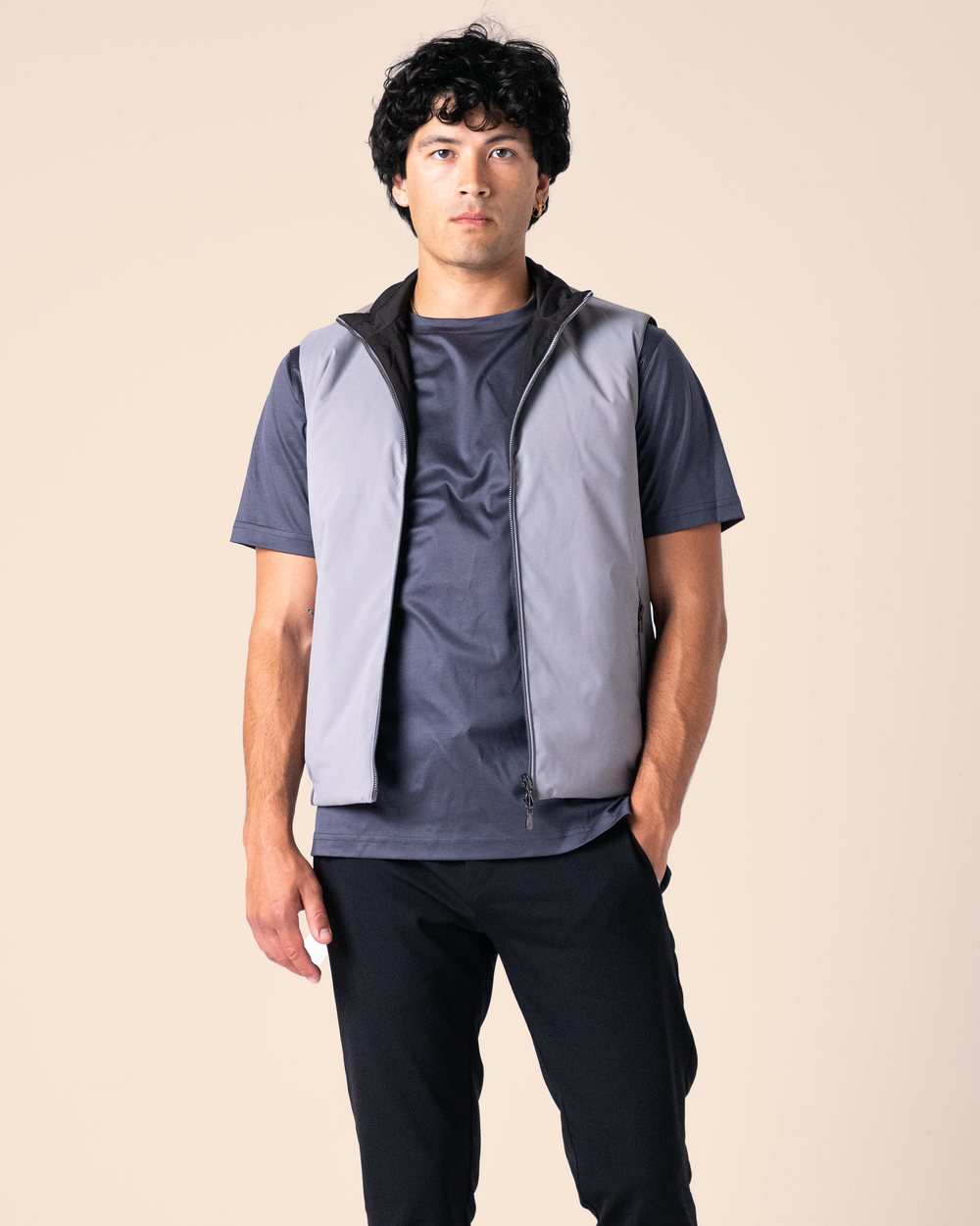 Man wearing a gray vest over a dark shirt on a beige background
