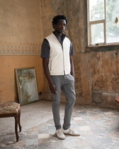 Man wearing a white vest over a dark shirt in an old, rustic room with peeling paint and a window.